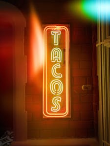 Bright neon tacos sign illuminated on a rustic brick wall at night, perfect for dining or street photography.